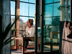 Woman reading with a coffee in a sunroom with dark framed glass walls