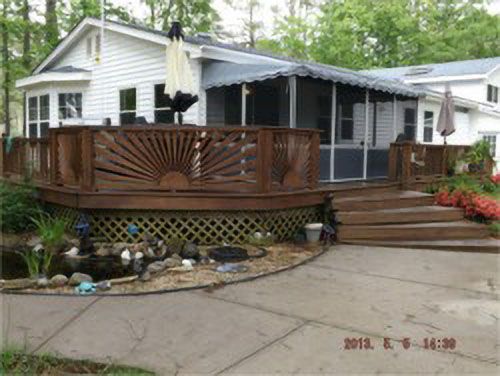 Screen room on a raised deck with a decorative sunburst railing beside a white house