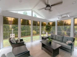 Sunroom interior with a vaulted white ceiling, ceiling fan and wicker seating
