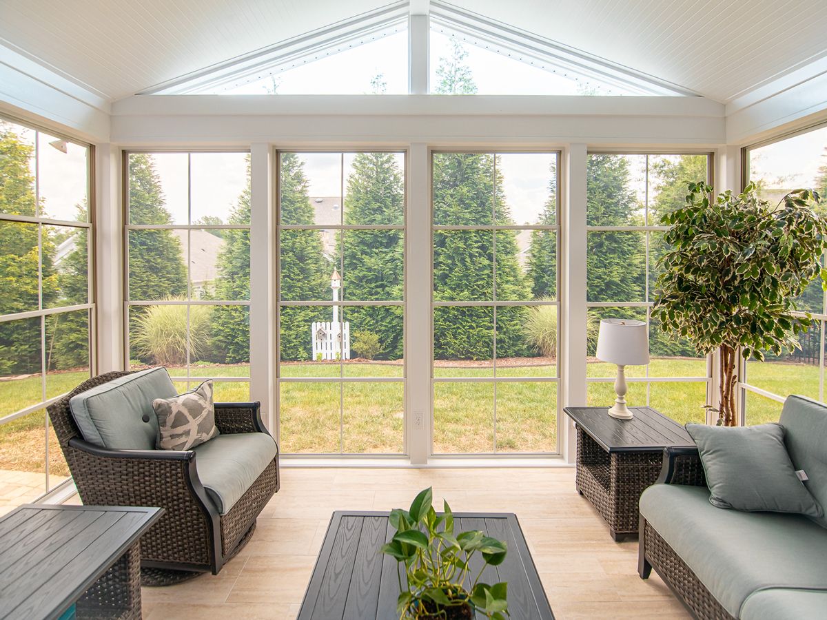 Sunroom interior with a vaulted ceiling and wicker seating overlooking a lawn
