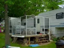 Screen room with clear vinyl panels on a raised deck beside a caravan