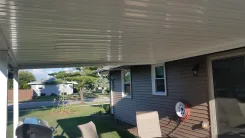 Underside of a white flat pan patio cover beside a sided house