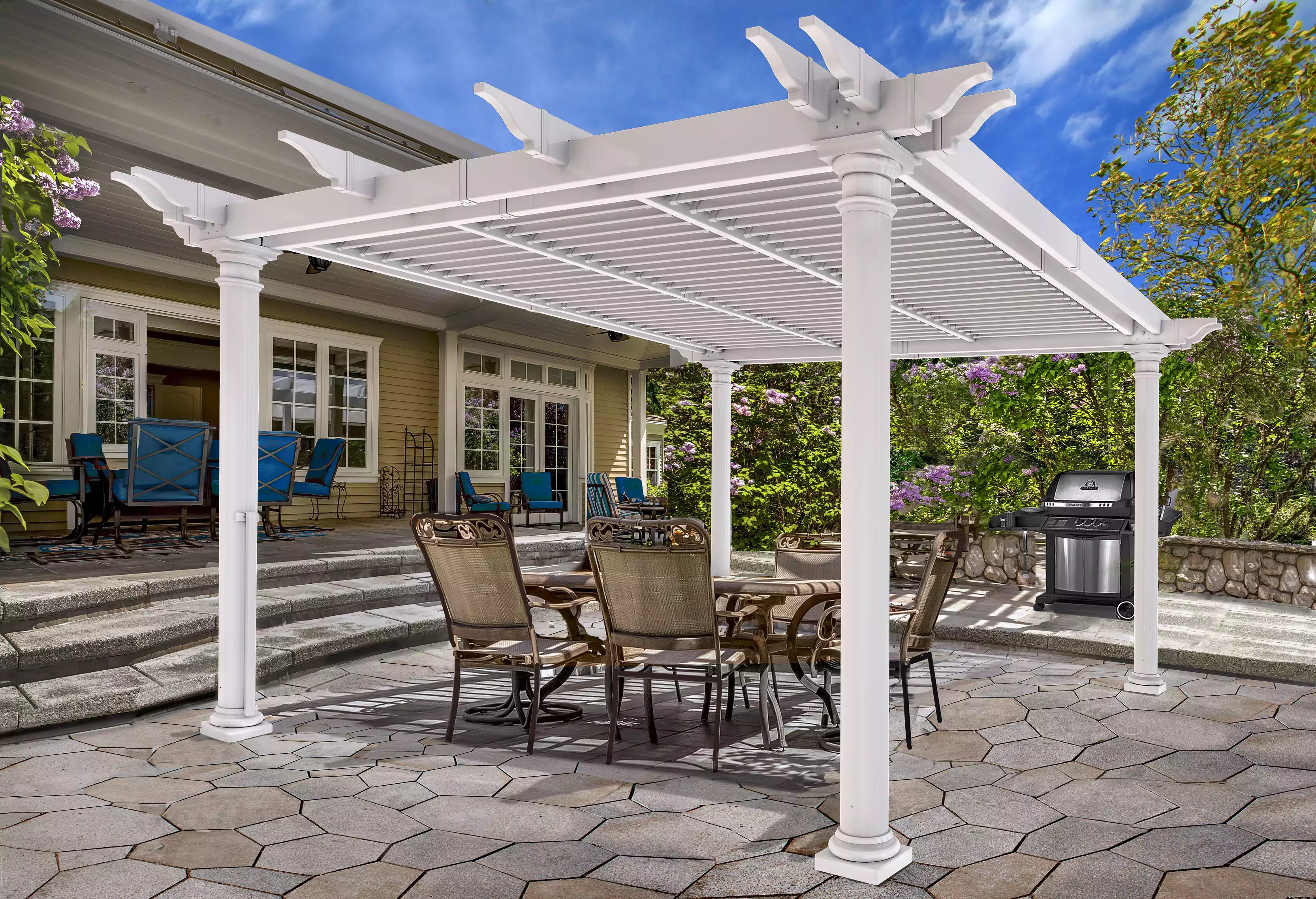 White louvred pergola over a stone patio dining area behind a house