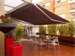 Dark retractable awning shading a rooftop terrace with tables and chairs