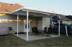 White flat pan patio cover over a patio dining set beside a sided house
