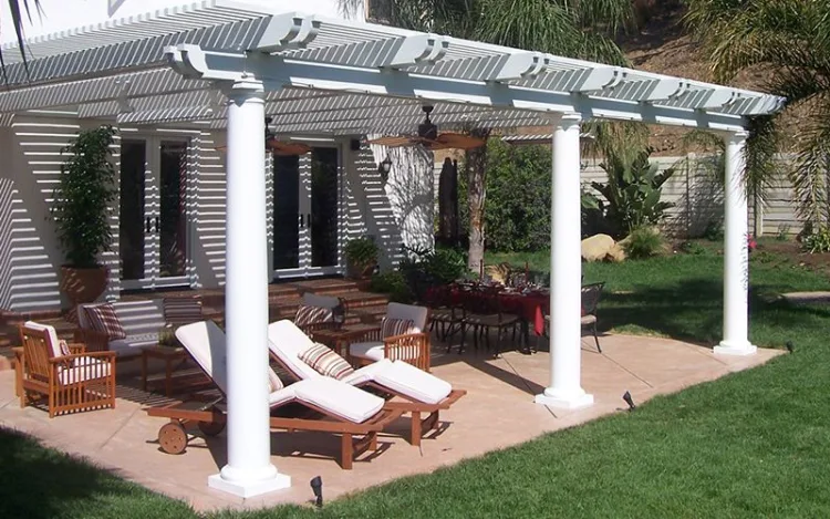 White pergola with louvred roof over a patio with sun loungers and dining furniture