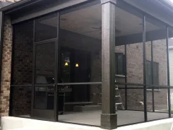 Screened porch with dark frames and brick columns over a patio with a barbecue