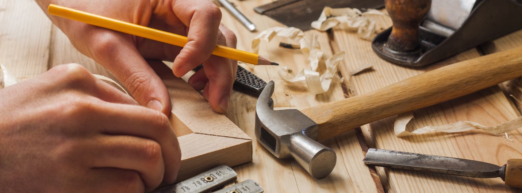 Hands sketching plans on paper surrounded by woodworking tools