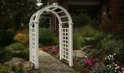 White arched arbour with lattice sides on a garden path beside a brick house