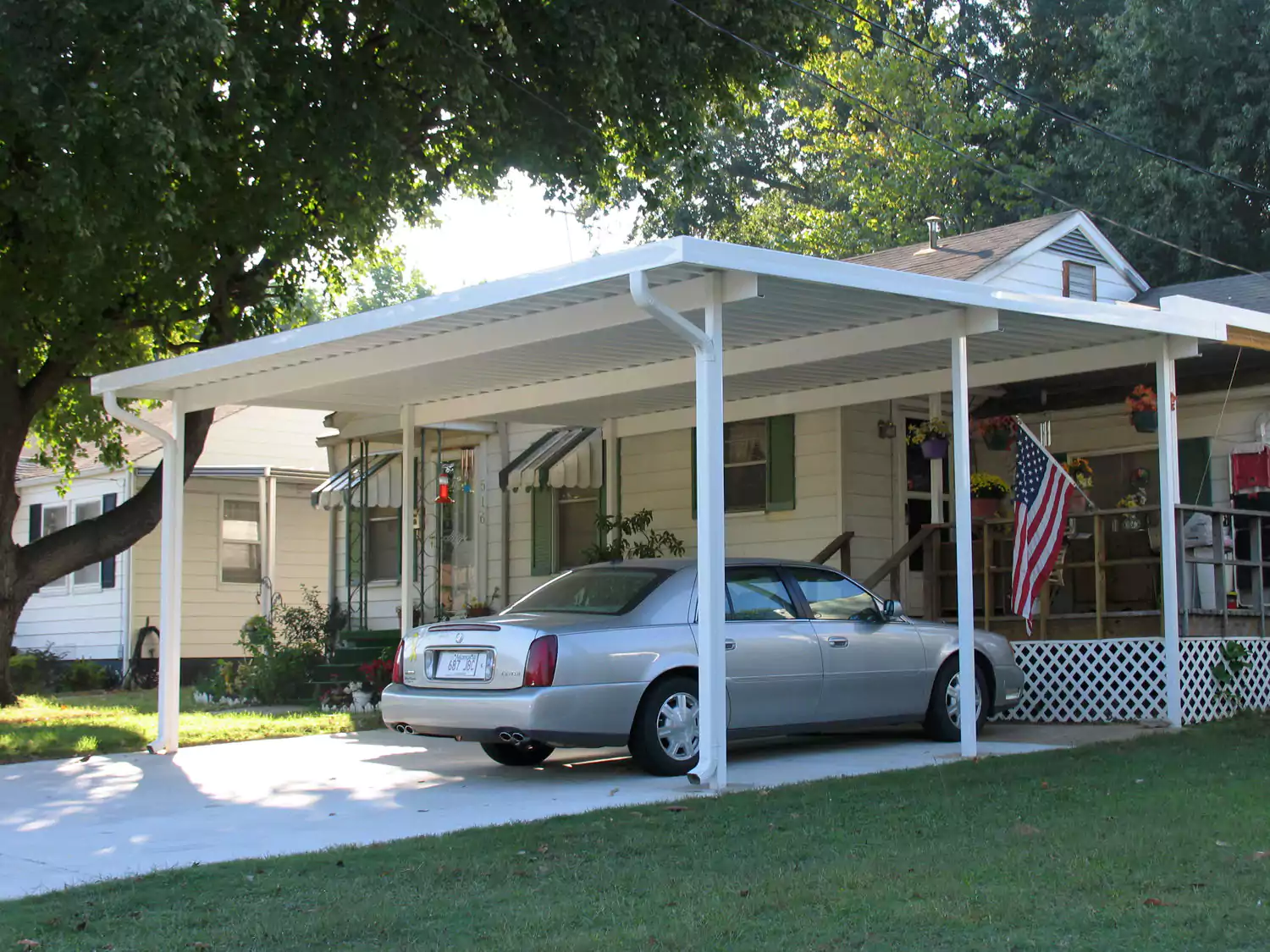 White patio cover and carport along the front of a house with a car parked beneath