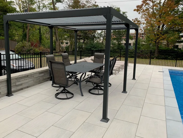 Dark grey aluminium louvred pergola over a paved poolside patio with a dining set
