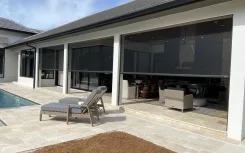 Motorised screens lowered across a covered patio opening beside a pool