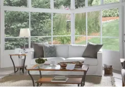 Sunroom interior with white framed windows, a sofa and coffee table looking onto a garden
