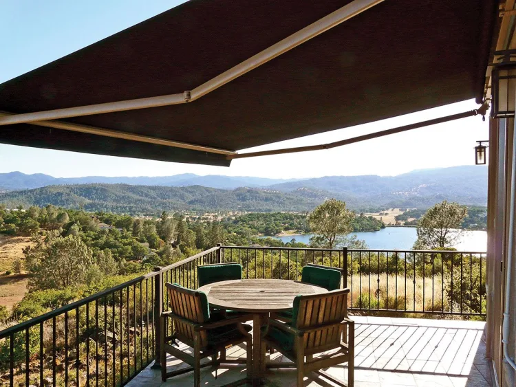 Retractable awning over a hillside deck with a table and lake view