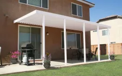 White patio cover along the back of a stucco house over a paved patio