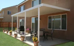 White patio cover along the back of a stucco house with a dining set and potted plants