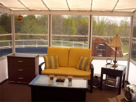 Inside a screen room with a yellow sofa, side table and pool view