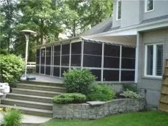Taupe soft top screen room attached to a brick home above a stone retaining wall