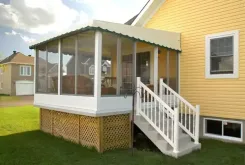 Polaria screen room with a green roof and white steps up to the door beside a yellow house