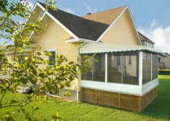 Polaria screen room with a green scalloped roof and lattice skirting beside a yellow house