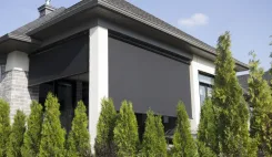 Solar shades lowered across a covered patio beside conifers