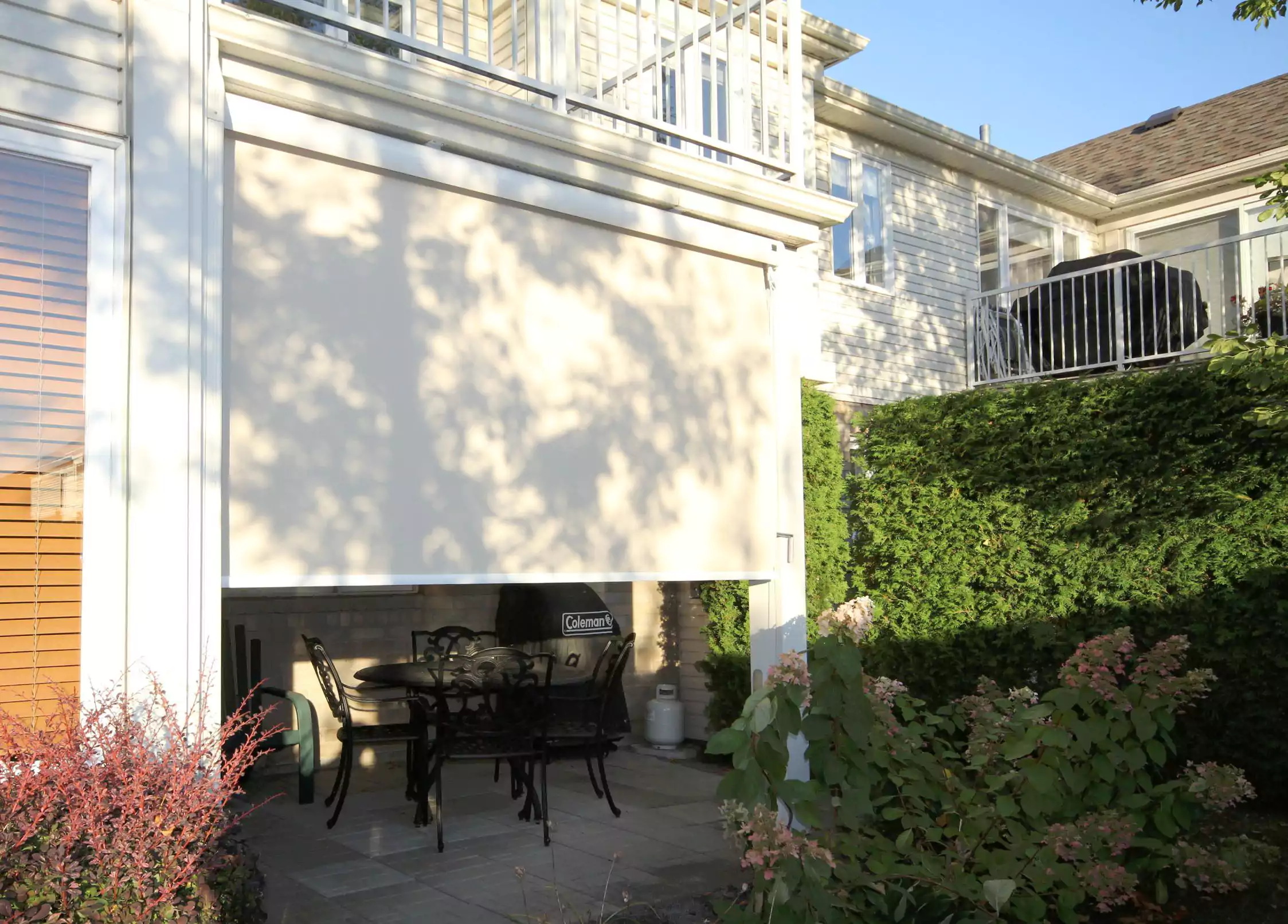 Solar shade lowered over a patio dining area beside a house