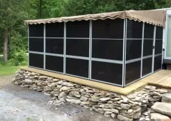 Screen room with a tan canopy roof and dark screens beside a caravan on a stone base