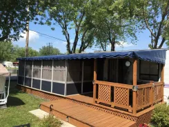 Screen room with a navy awning roof along a caravan with a wooden deck and steps