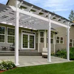 White pergola along the back of a house shading a paved patio