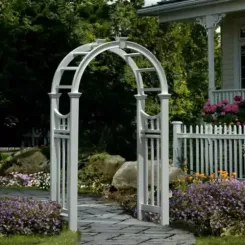 White vinyl arched arbour on a paved path beside a picket fence
