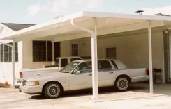 White W pan carport sheltering a 1960s car beside a house